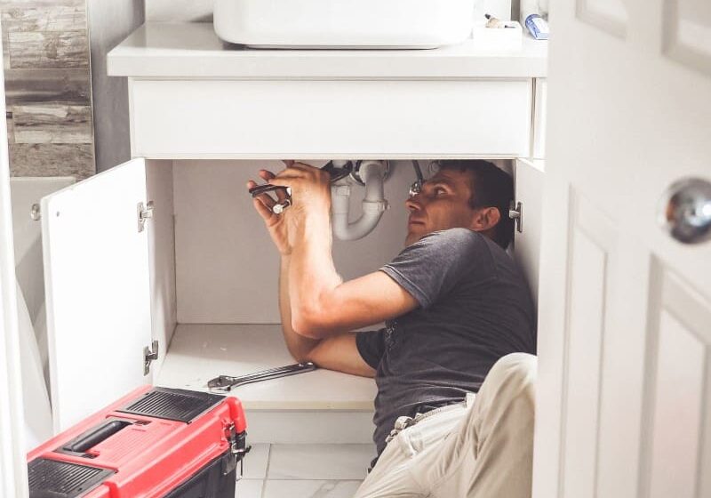 Plumber repairing sink under cabinet.